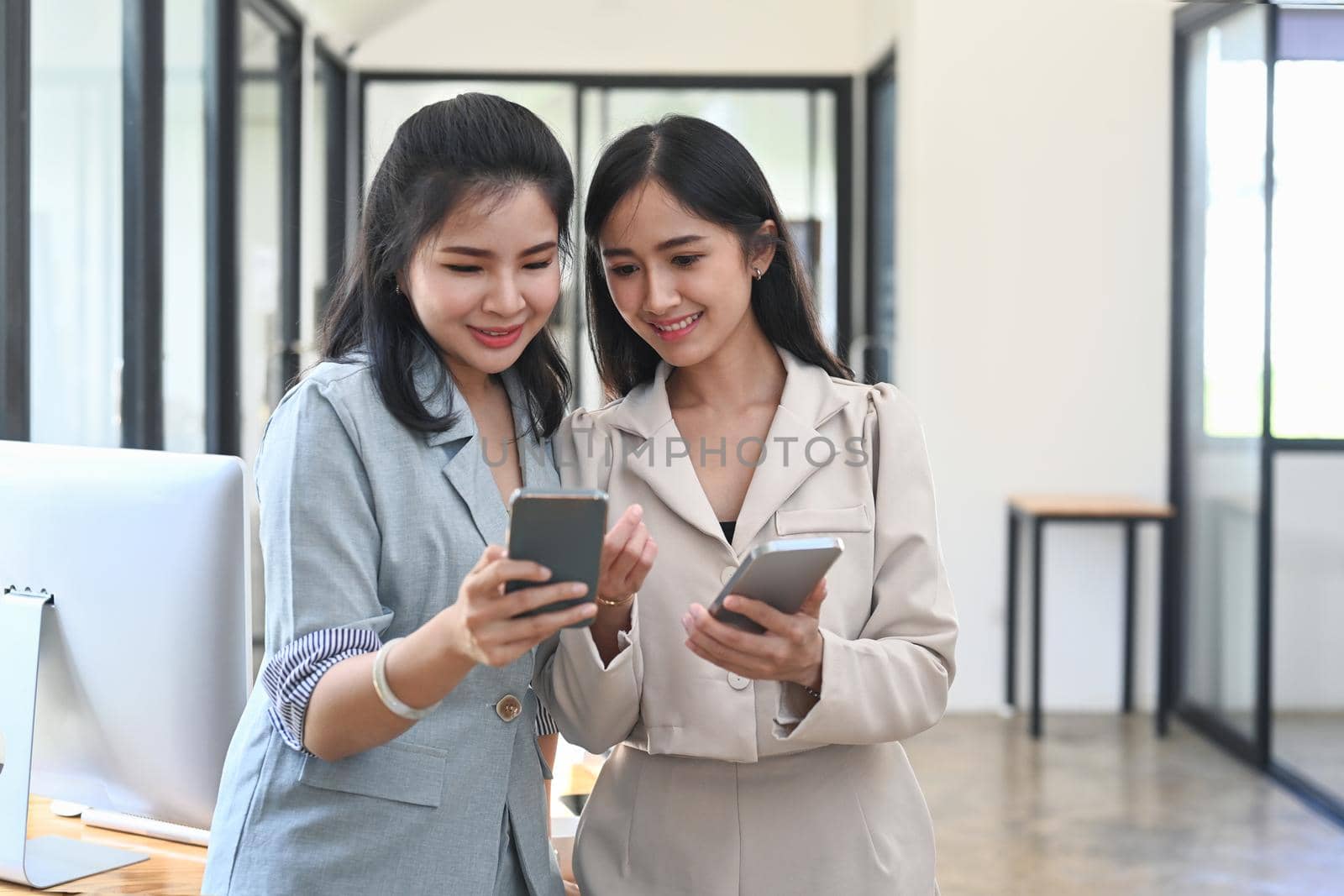 Two young businesswoman taking a break in office and using smart phone for checking social media. by prathanchorruangsak