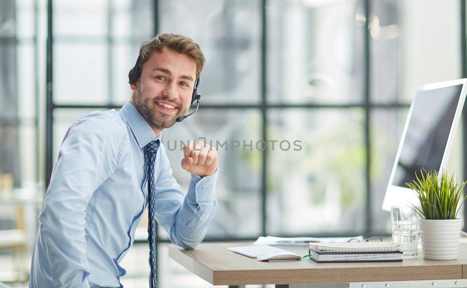 Young handsome male customer support phone operator with headset working in his office