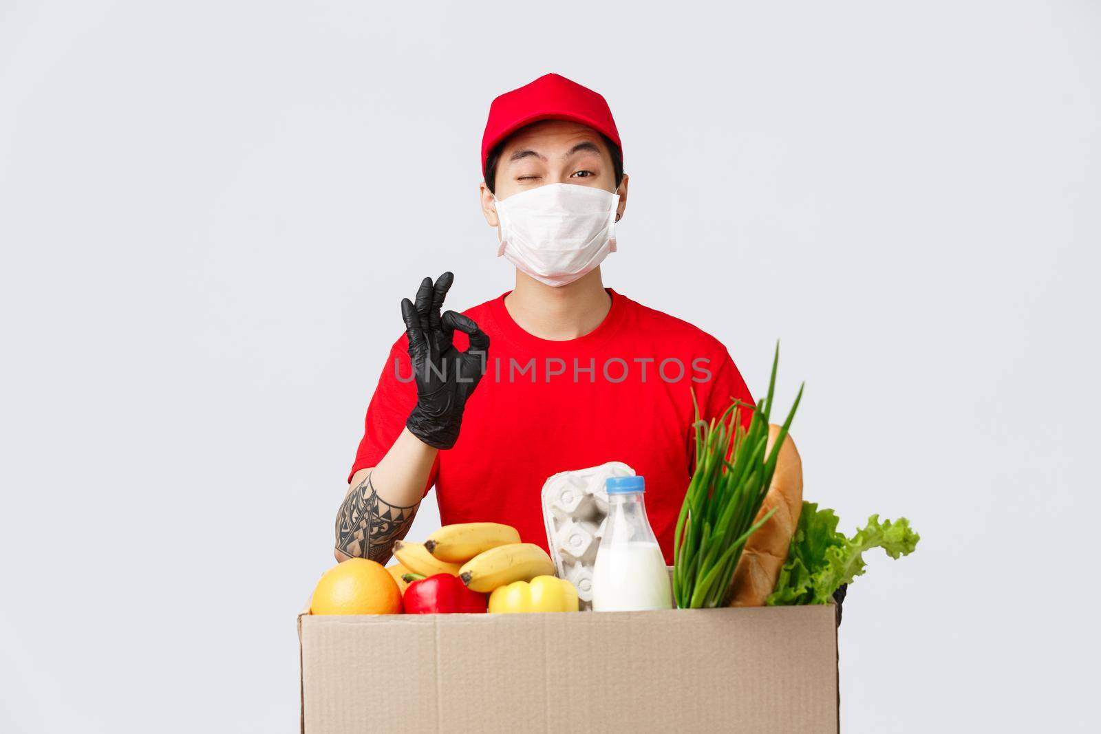 Online shopping, food delivery and coronavirus pandemic concept. Smiling asian courier in uniform show okay sign, give client his order, fresh groceries from online shop, wear medical mask.