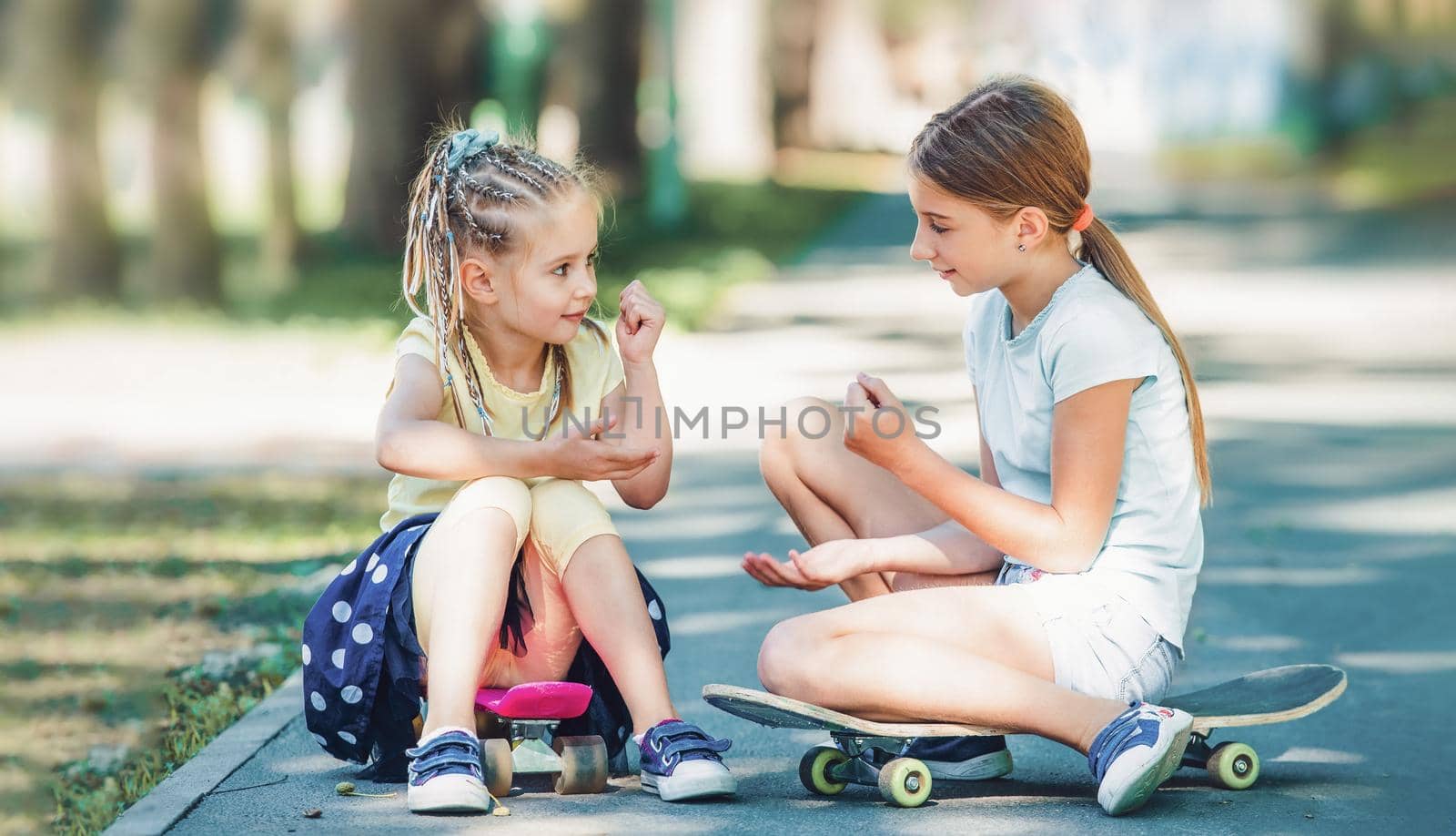 Beautiful little girls sitting on skateboards in the park and playing together in summertime