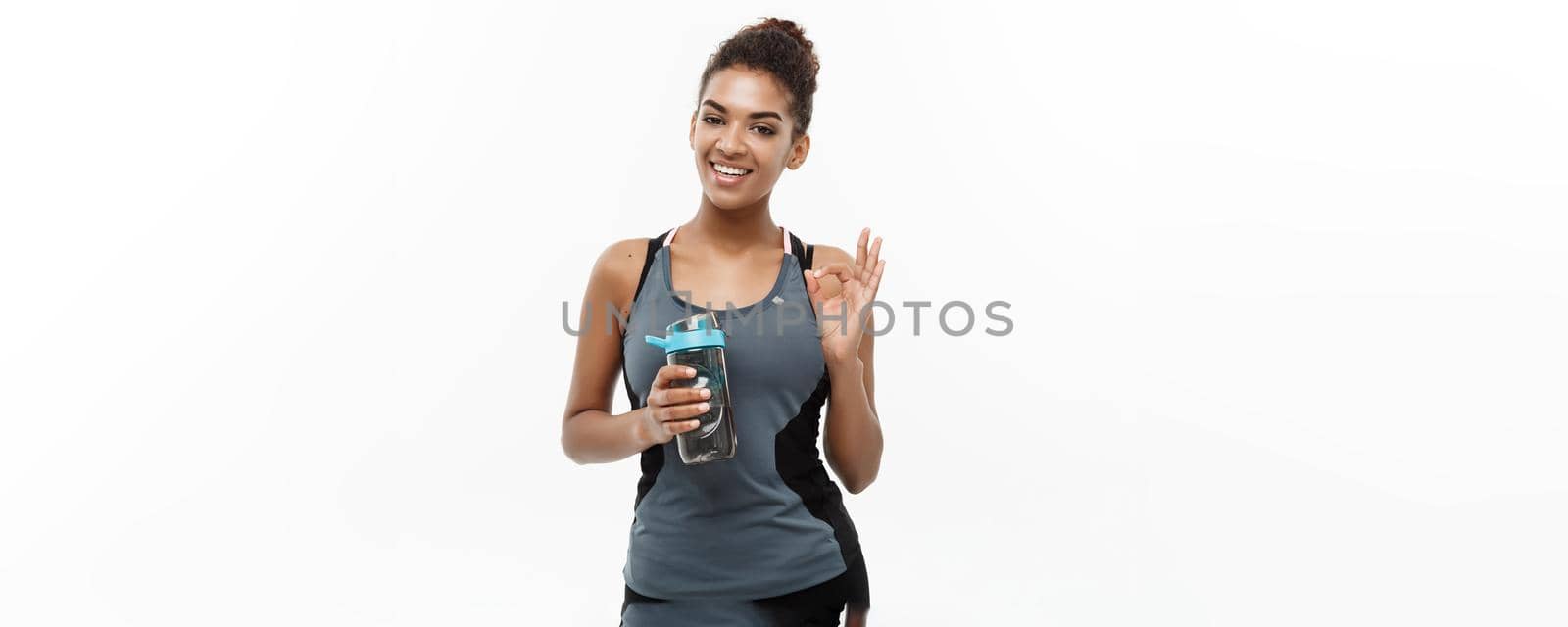 Healthy and Fitness concept - beautiful African American girl in sport clothes holding water bottle after workout. Isolated on white studio background by Benzoix