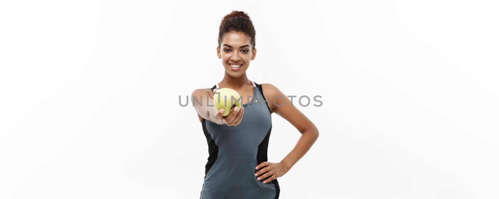 Healthy and Fitness concept - Beautiful American African lady in grey fitness clothes holding green apple. Isolated on white background. by Benzoix