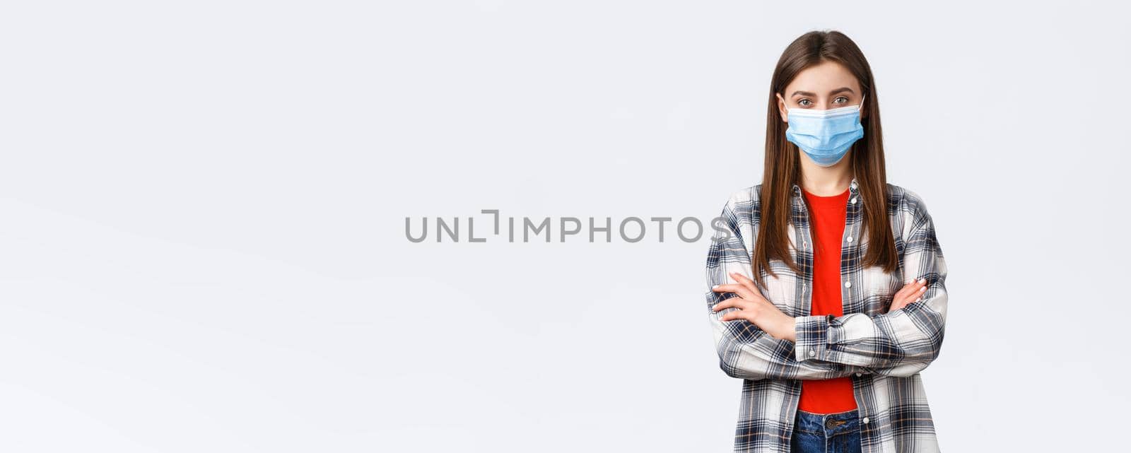 Coronavirus outbreak, leisure on quarantine, social distancing and emotions concept. Confident young woman in checked shirt wear medical mask, cross arms chest, determined look camera.