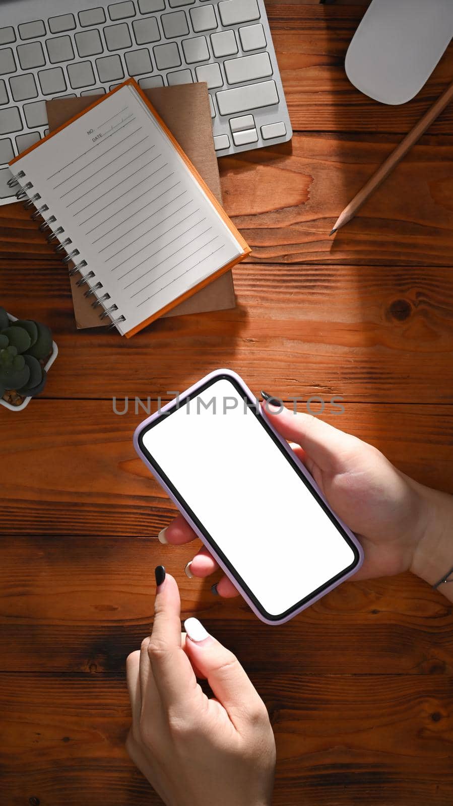 Above view woman holding mobile phone with white empty screen on wooden table.