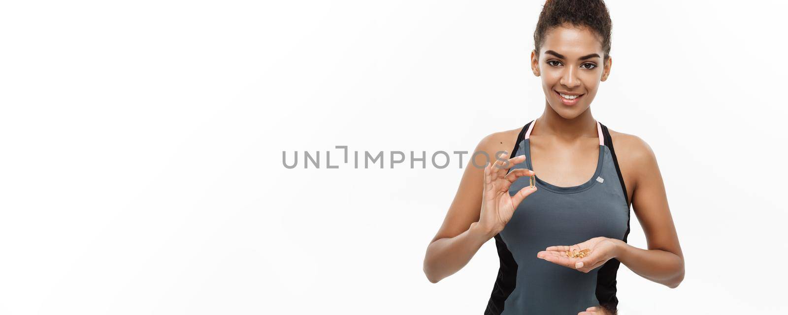 Healthy and Fitness concept - Closeup portrait of beautiful African American taking a pill of Cod liver oil. Isolated on white studio background. by Benzoix