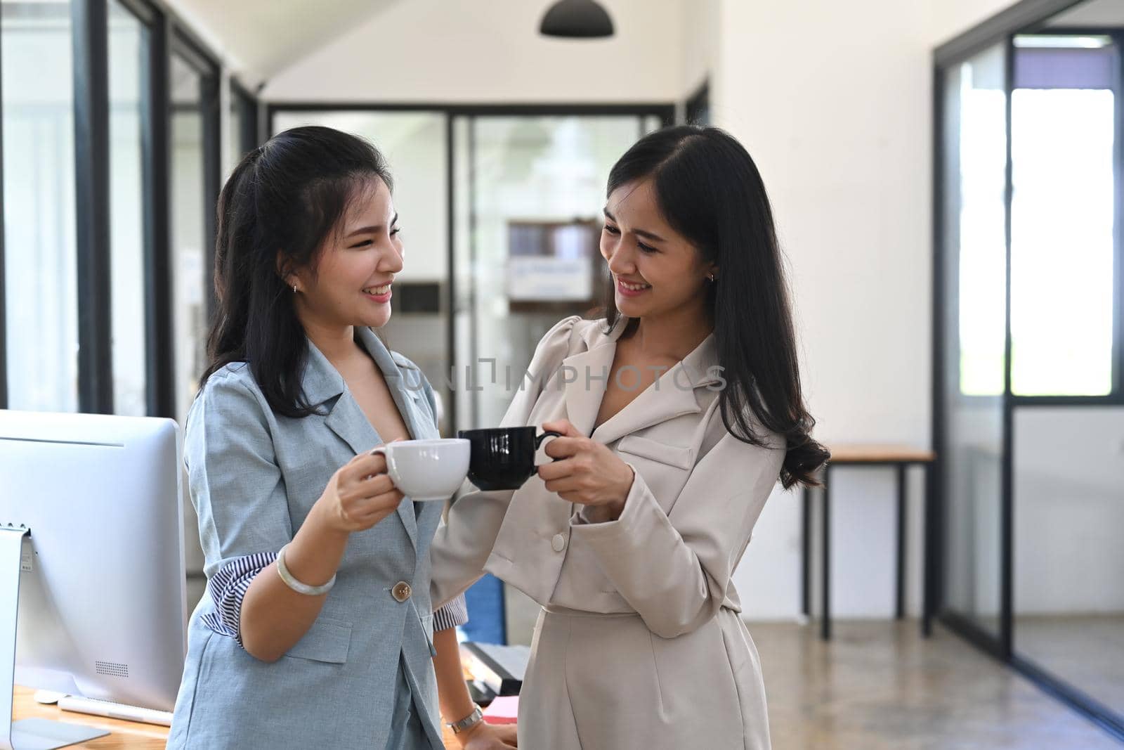 Two business women discussing project or sharing news during coffee break in office. by prathanchorruangsak