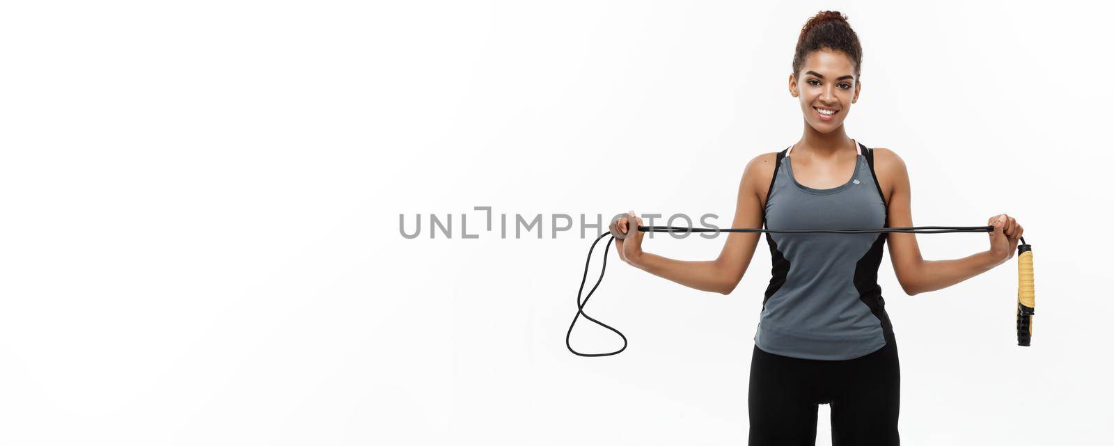 Sport, training, lifestyle and Fitness concept - portrait of beautiful happy African American woman exercising with jumping rope. Isolated on white studio background