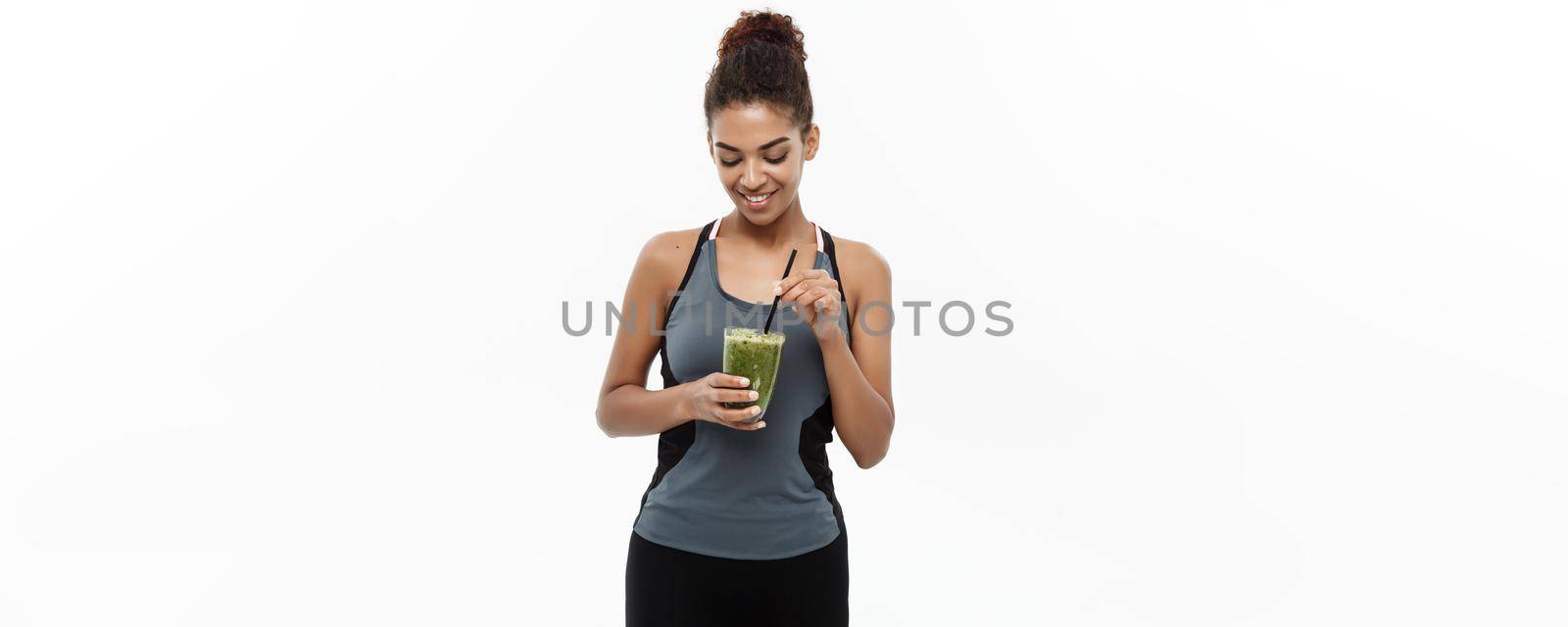 Healthy and Fitness concept - Beautiful American African lady in fitness clothing drinking healthy vegetable drink. Isolated on white background. by Benzoix