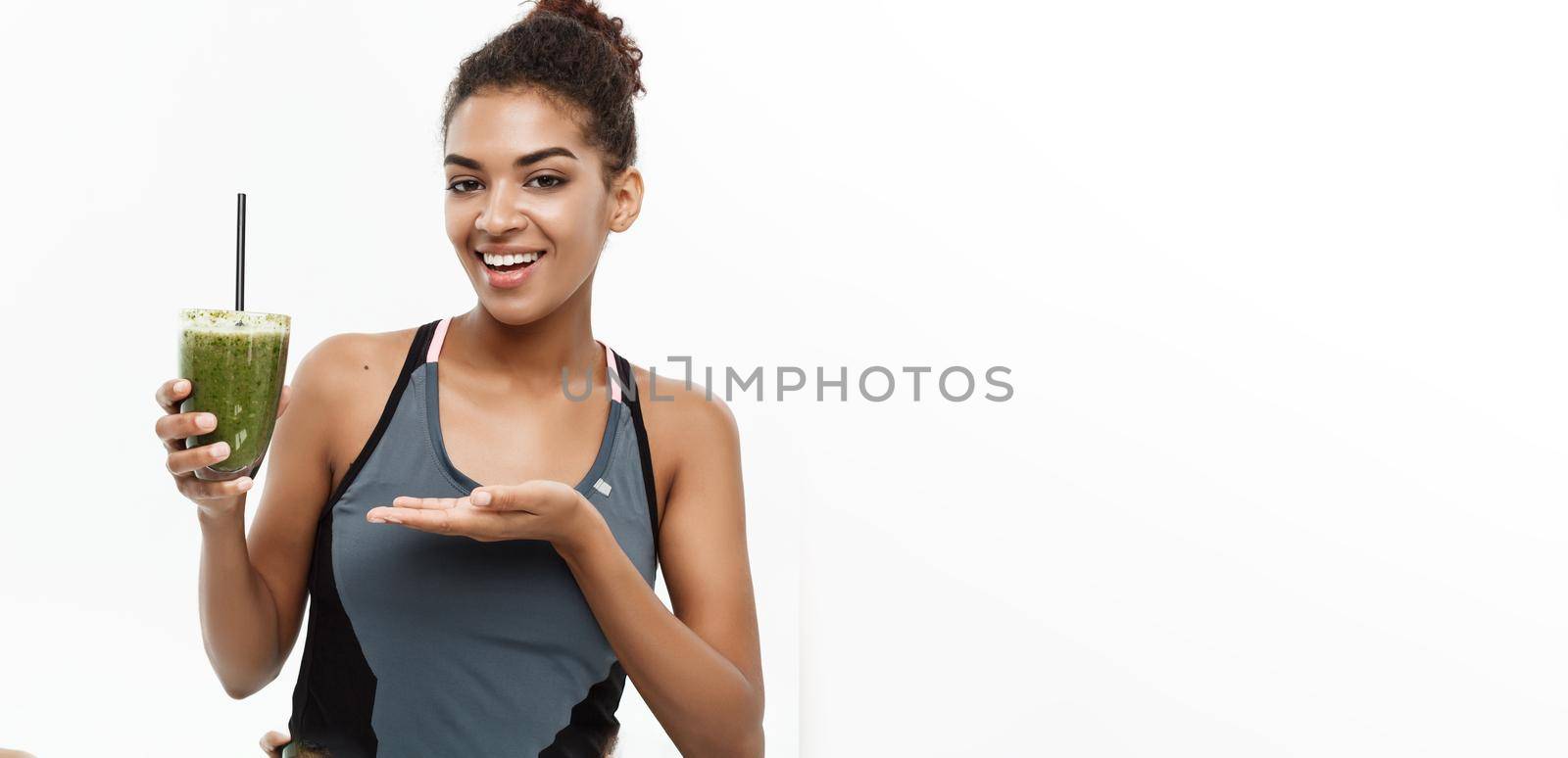 Healthy and Fitness concept - Beautiful American African lady in fitness clothing drinking healthy vegetable drink. Isolated on white background. by Benzoix