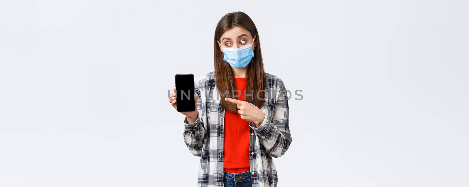 Different emotions, covid-19, social distancing and technology concept. Excited and enthusiastic good-looking girl in medical mask, pointing looking at mobile phone display, promote app by Benzoix