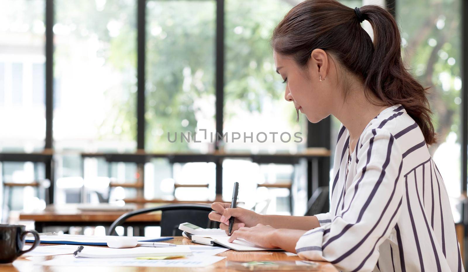 Asian female accountant making calculations. Savings, finances and economy concept through a laptop. by wichayada