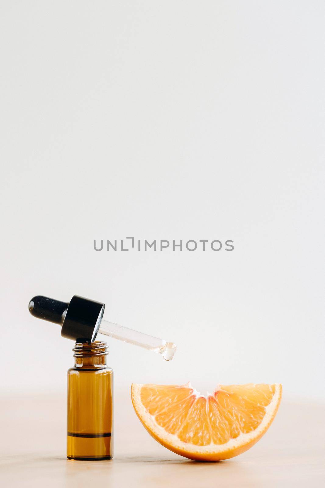 Essential oil in one bottle and a piece of orange standing on the surface by Lobachad