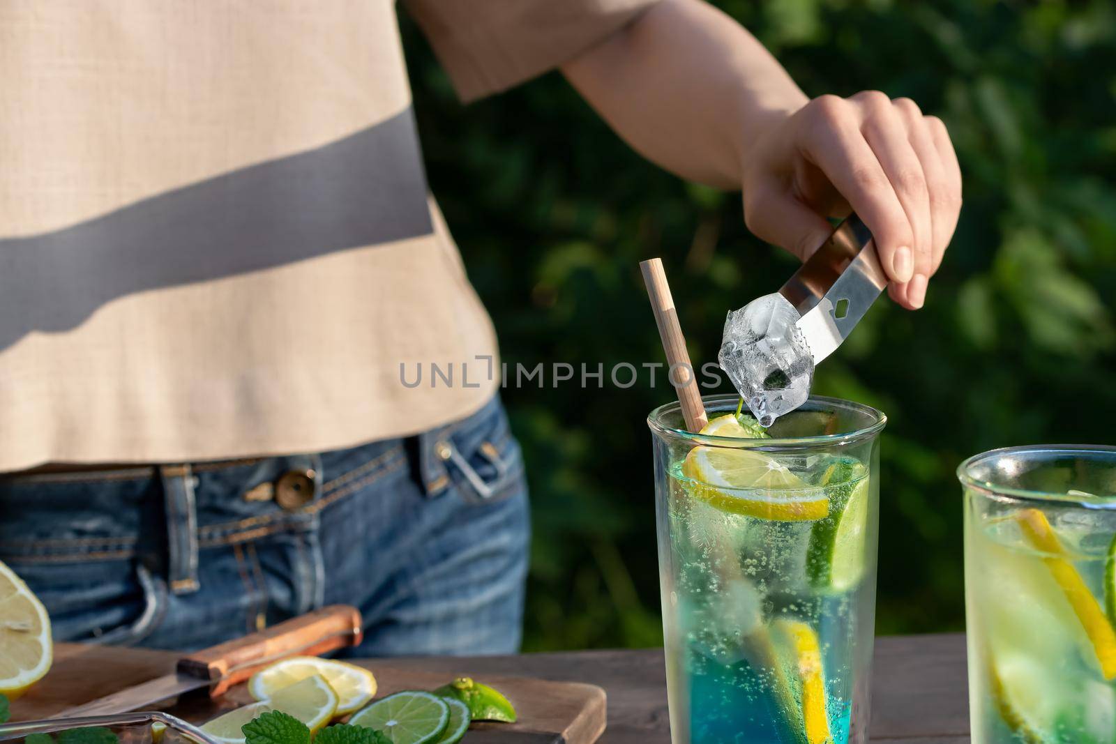 Girl makes summer refreshing cocktails blue lagoon. Close-up of adding ice cubes to glasses. Selective focus by galsand