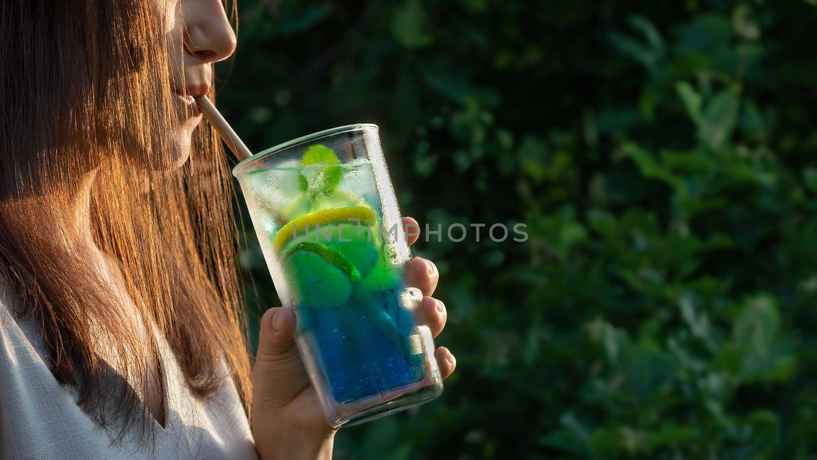 Young woman with long dark hair drinking a summer refreshing cocktail through a straw. Selective focus.