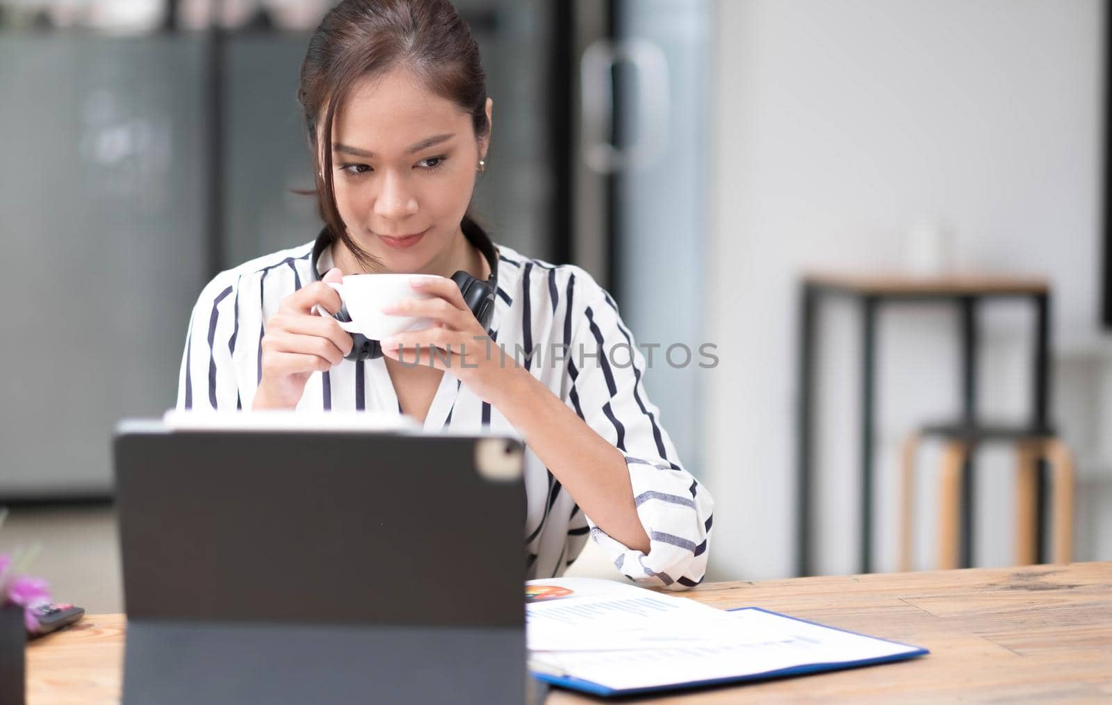 Image of a young woman smiling through a laptop's web camera while holding a cup of coffee in the kitchen at home..