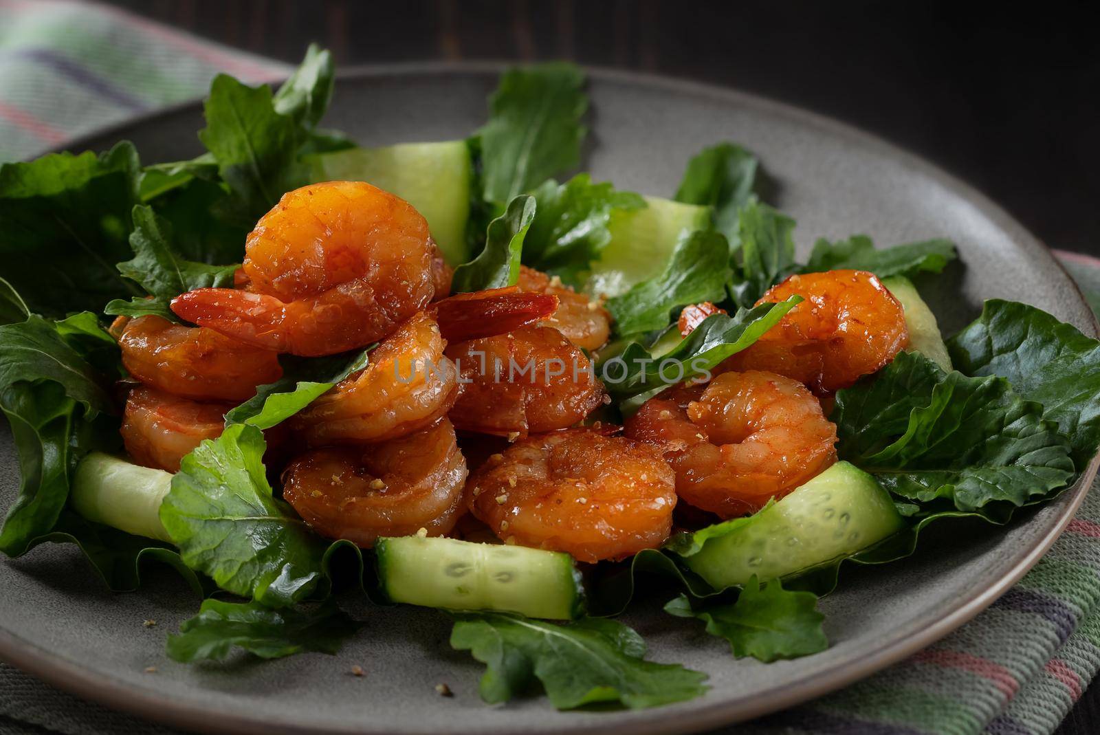 Fresh salad with grilled prawns, cucumbers and arugula beautifully served on a plate.