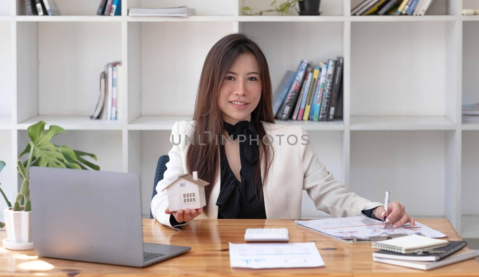 Miniature house in the hands of an Asian woman real estate agent home loan working at the office. Looking at the camera..