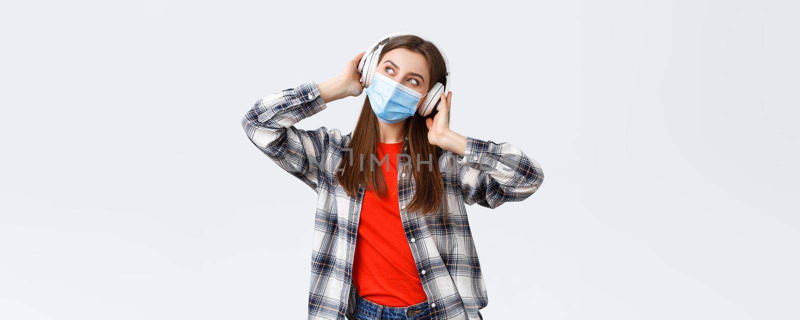 Social distancing, leisure and lifestyle on covid-19 outbreak, coronavirus concept. Happy carefree attractive girl in medical mask, look away dreamy, imaging while listening music in headphones.