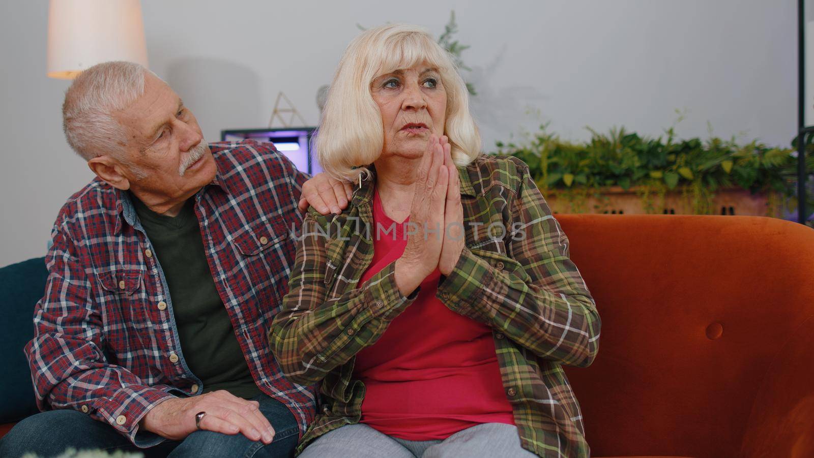 Senior elderly family couple grandparents man woman pray with hope, looking upward and making wish, asking with hopeful imploring expression, begging apology. Mature grandmother grandfather at home