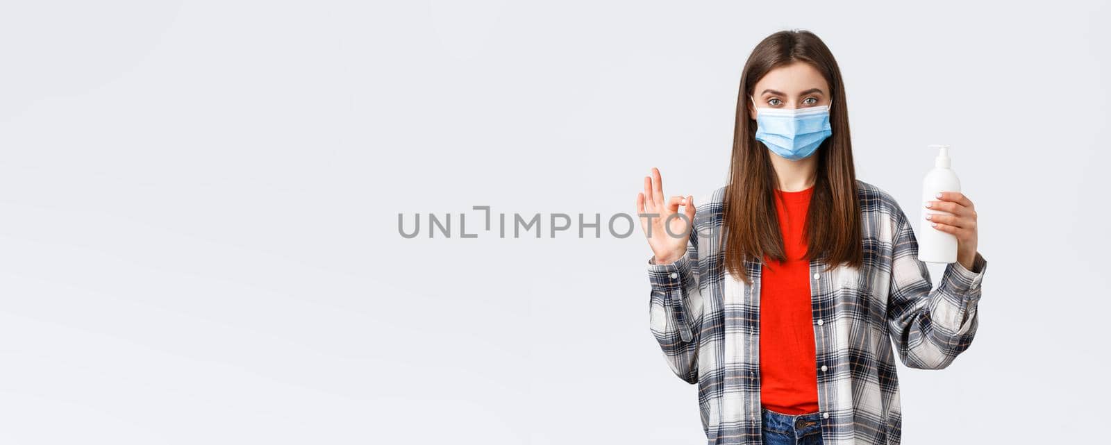 Coronavirus outbreak, leisure on quarantine, social distancing and emotions concept. Self-assured young woman in medical mask recommend hand soap or sanitizer, show okay sign.