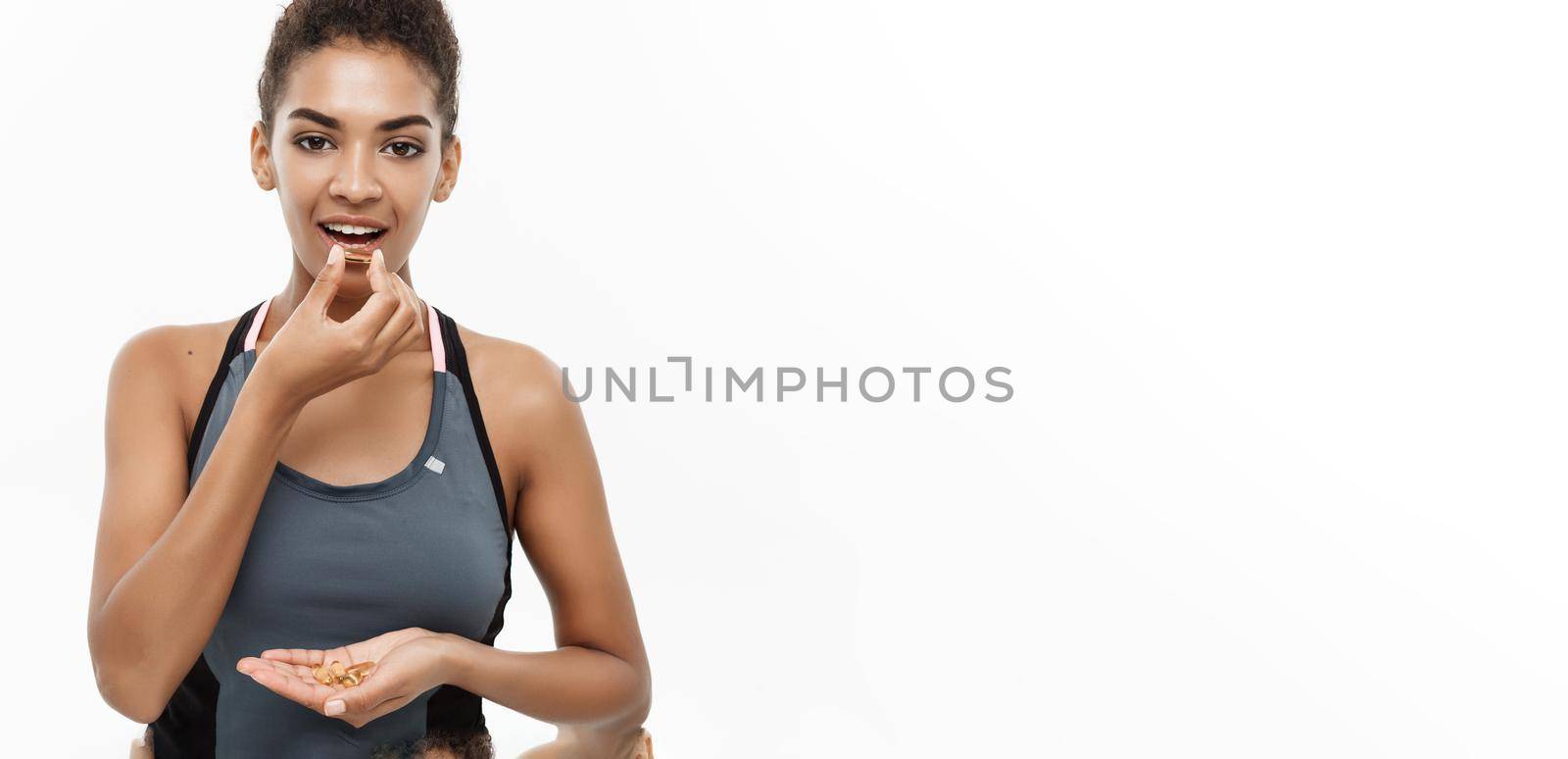 Healthy and Fitness concept - Closeup portrait of beautiful African American taking a pill of Cod liver oil. Isolated on white studio background. by Benzoix