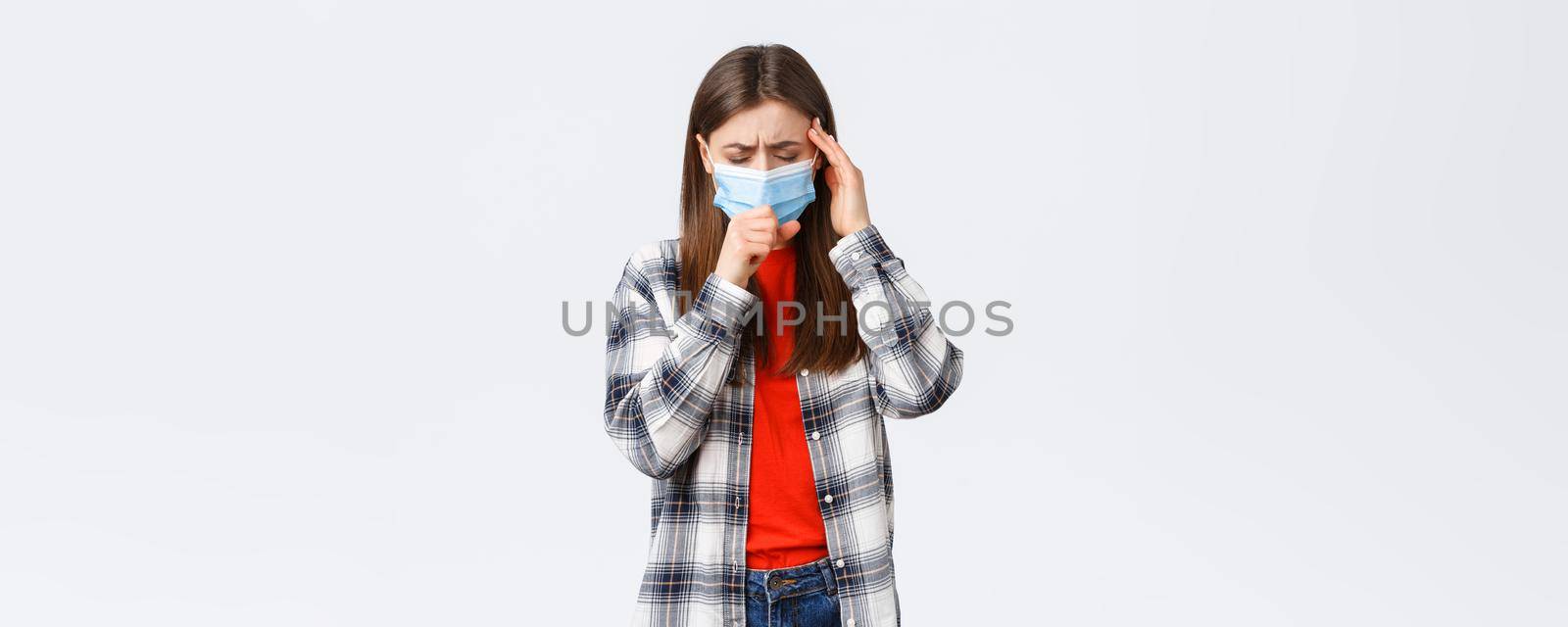 Coronavirus outbreak, leisure on quarantine, social distancing and emotions concept. Young woman feel sick, wear medical mask and coughing, touch temple as headache, high fever.