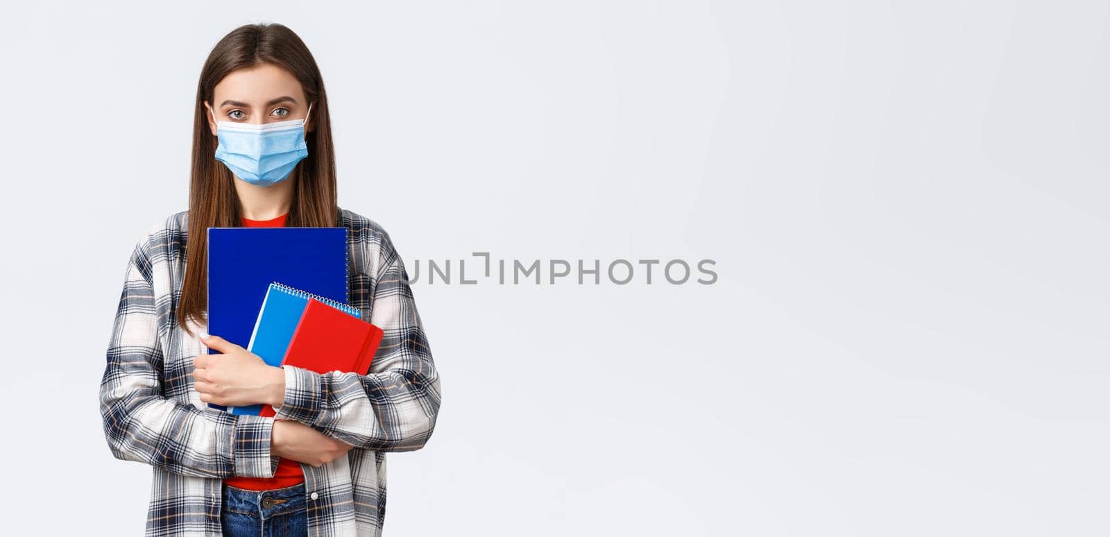 Coronavirus pandemic, covid-19 education, and back to school concept. Young female student in medical mask holding notebooks, going to class, freshman in university in personal protective facemask by Benzoix