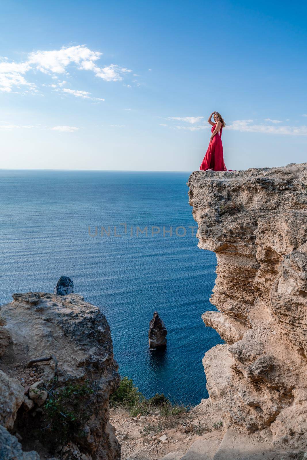 A woman in a red flying dress fluttering in the wind, against the backdrop of the sea