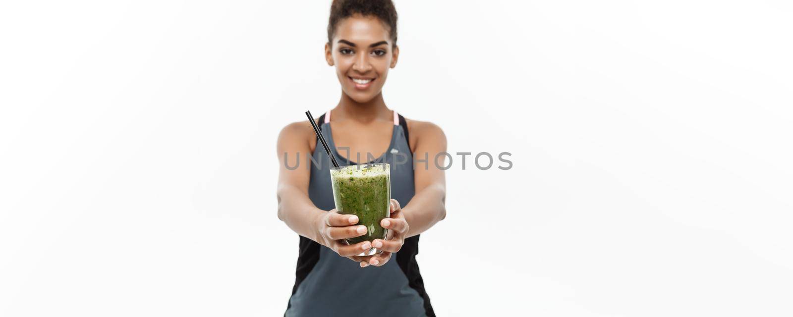 Healthy and Fitness concept - Beautiful American African lady in fitness clothing drinking healthy vegetable drink. Isolated on white background