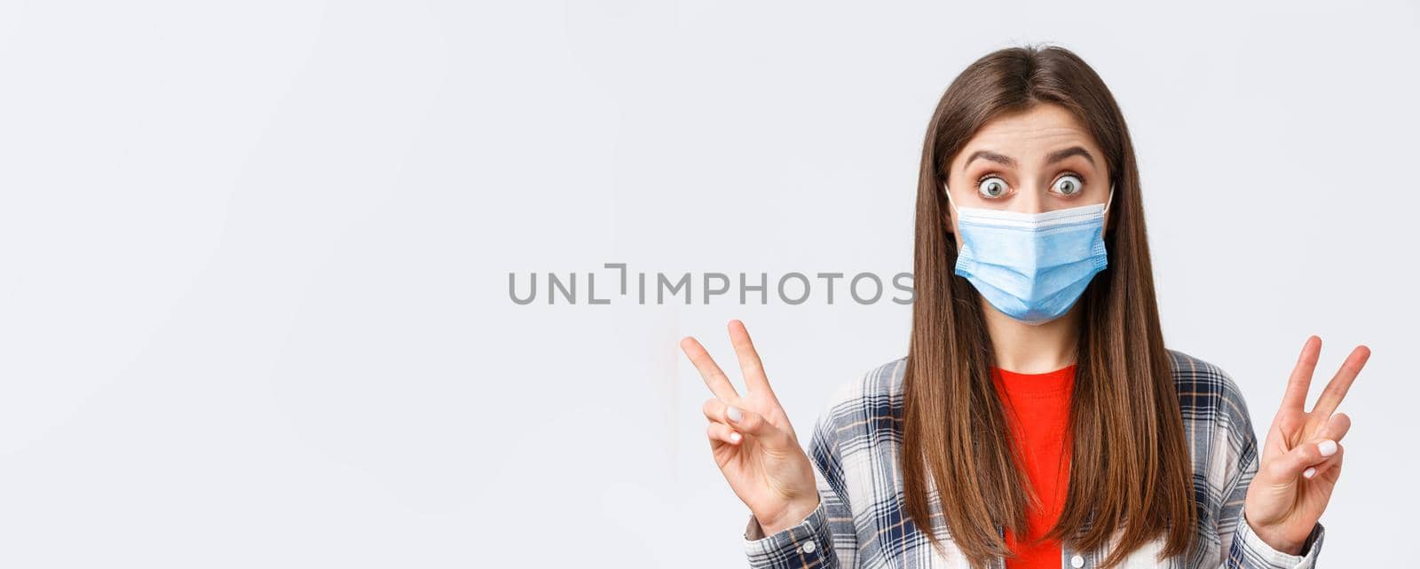Coronavirus outbreak, leisure on quarantine, social distancing and emotions concept. Close-up of excited and thrilled cute woman in medical mask, showing peace sign or quotes, stare impressed by Benzoix