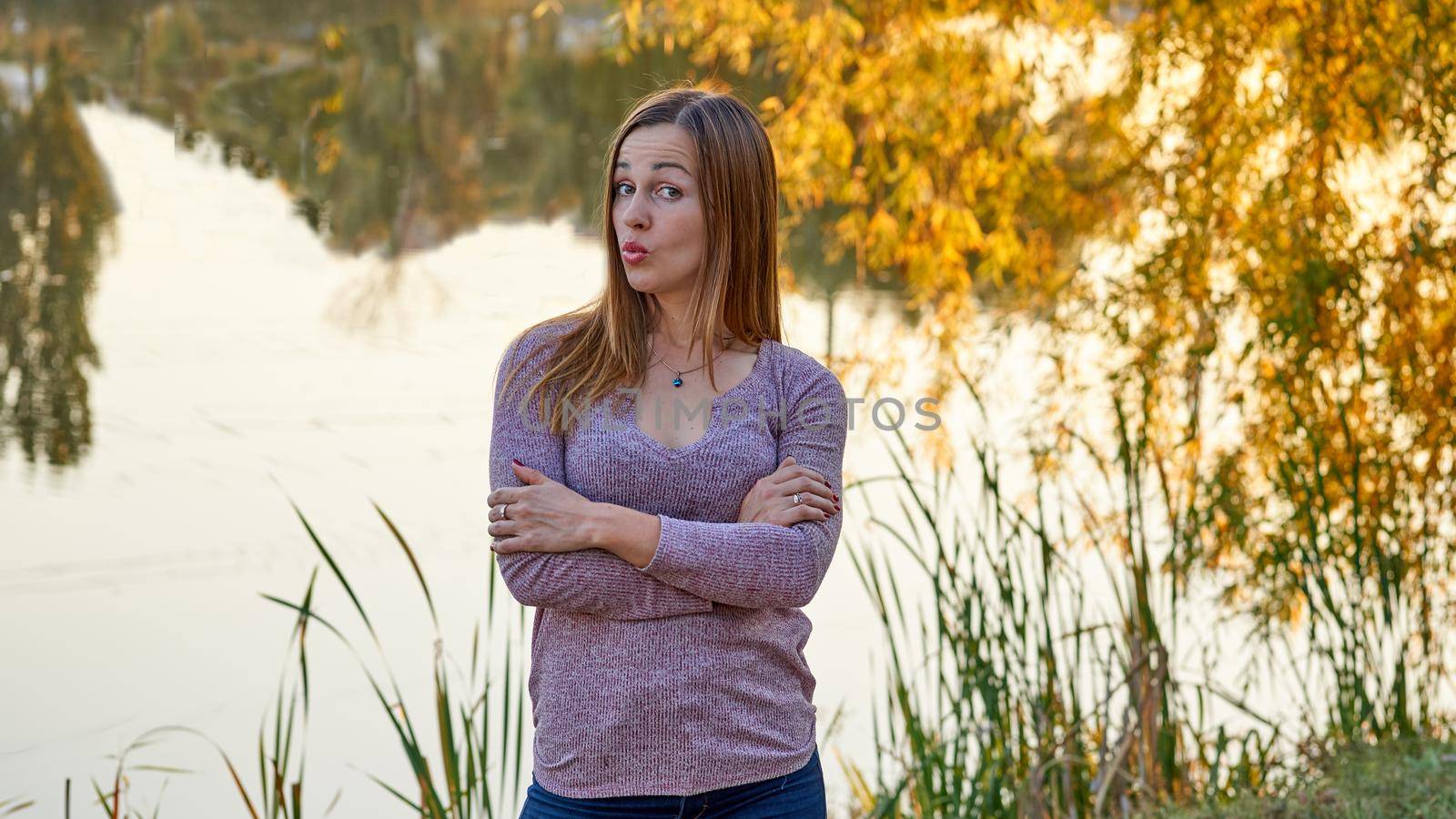 Young cheerful woman on the shore of a calm lake among golden autumn foliage by jovani68