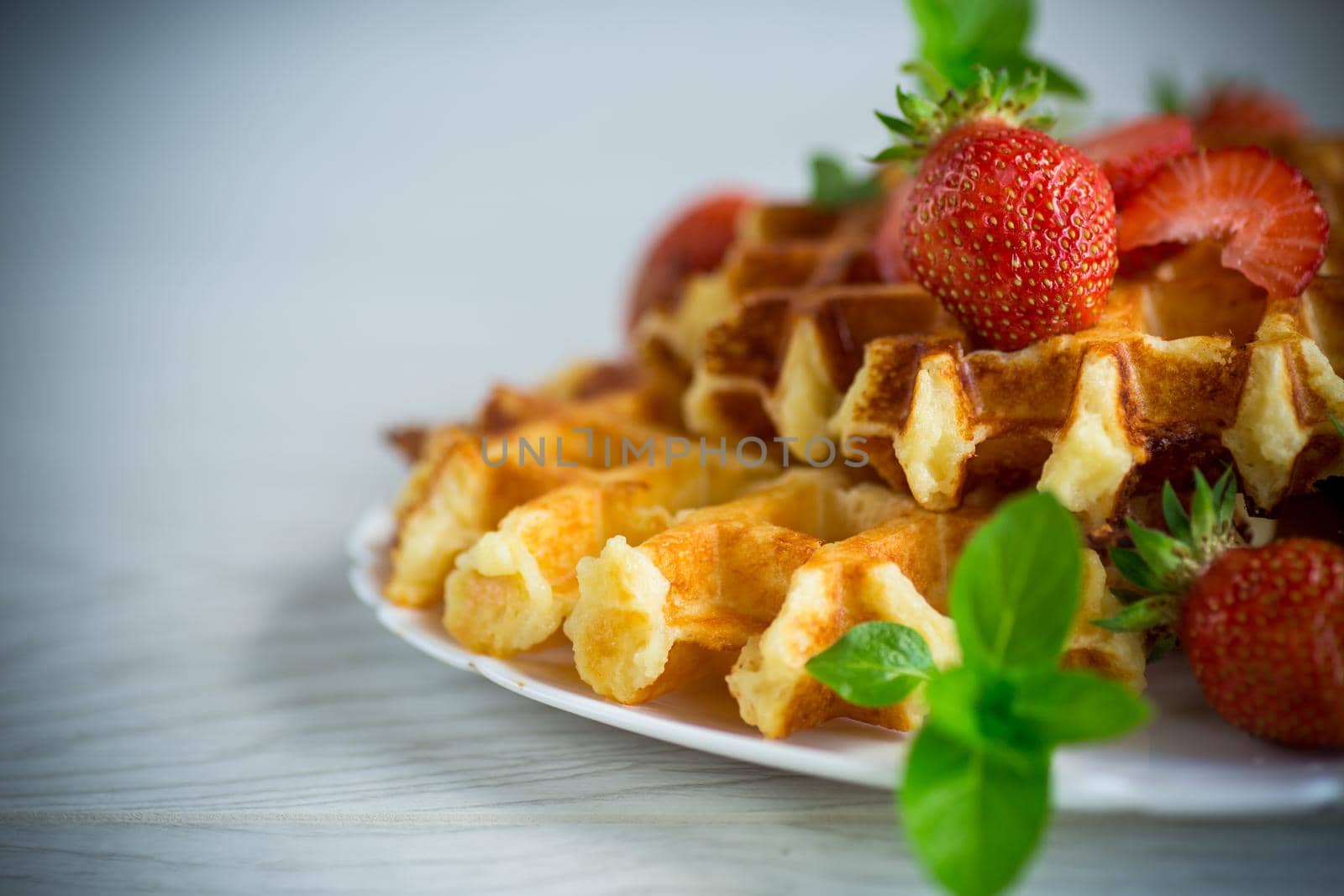 Sweet curd cooked waffles with fresh ripe strawberries, on a wooden table.