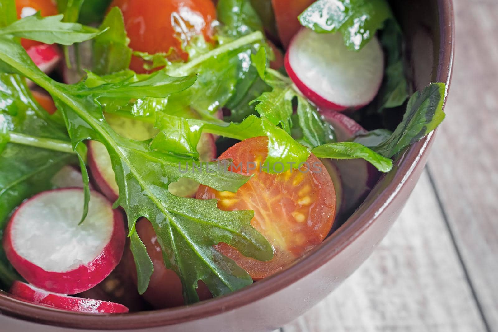 On the table in a ceramic plate salad of radishes, tomatoes, arugula. Presented close-up. The view from the top.