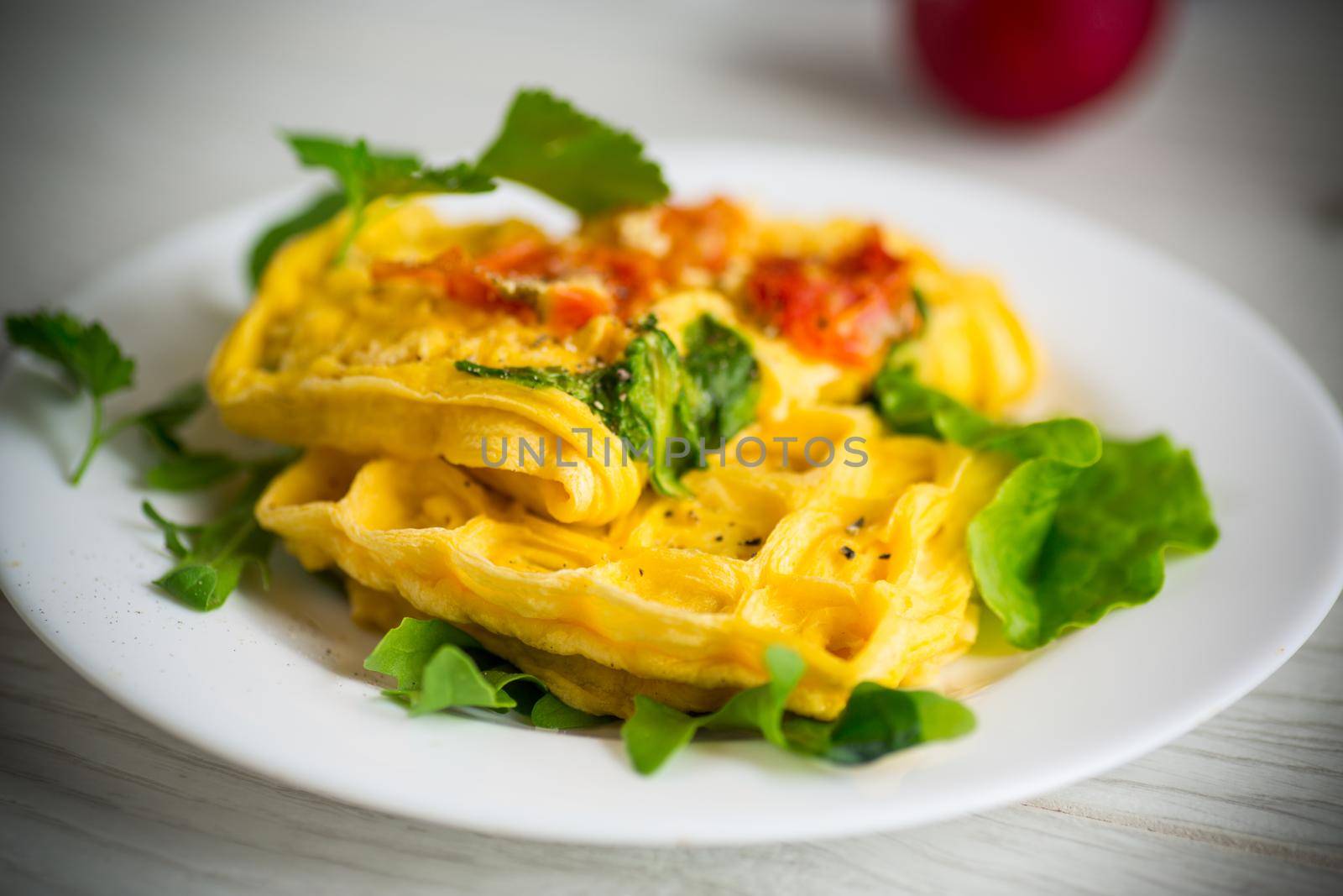 Egg omelet stuffed with tomato and greens fried in the form of waffles, on a wooden table.