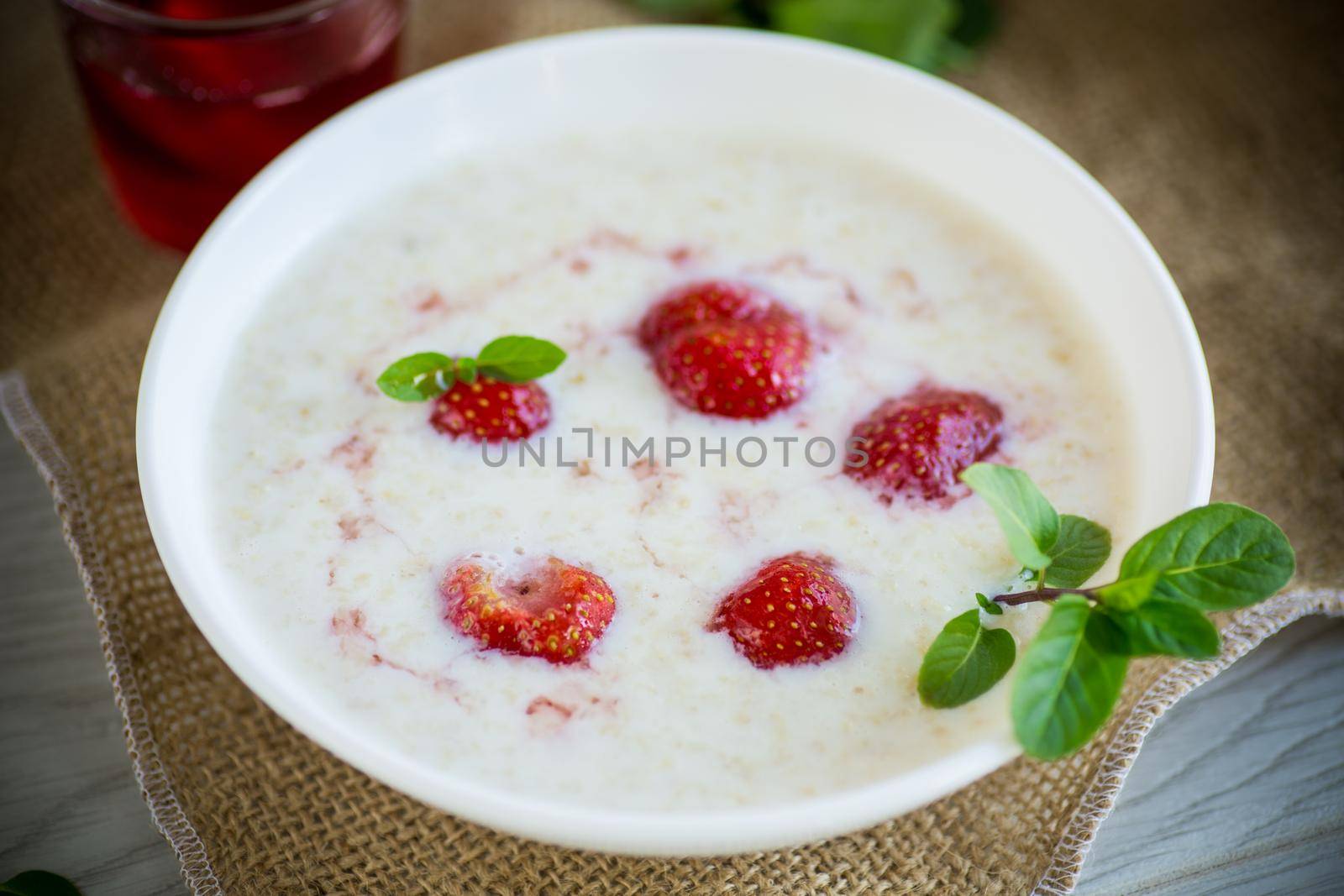 sweet milk oatmeal with strawberries in a plate, on a wooden table.