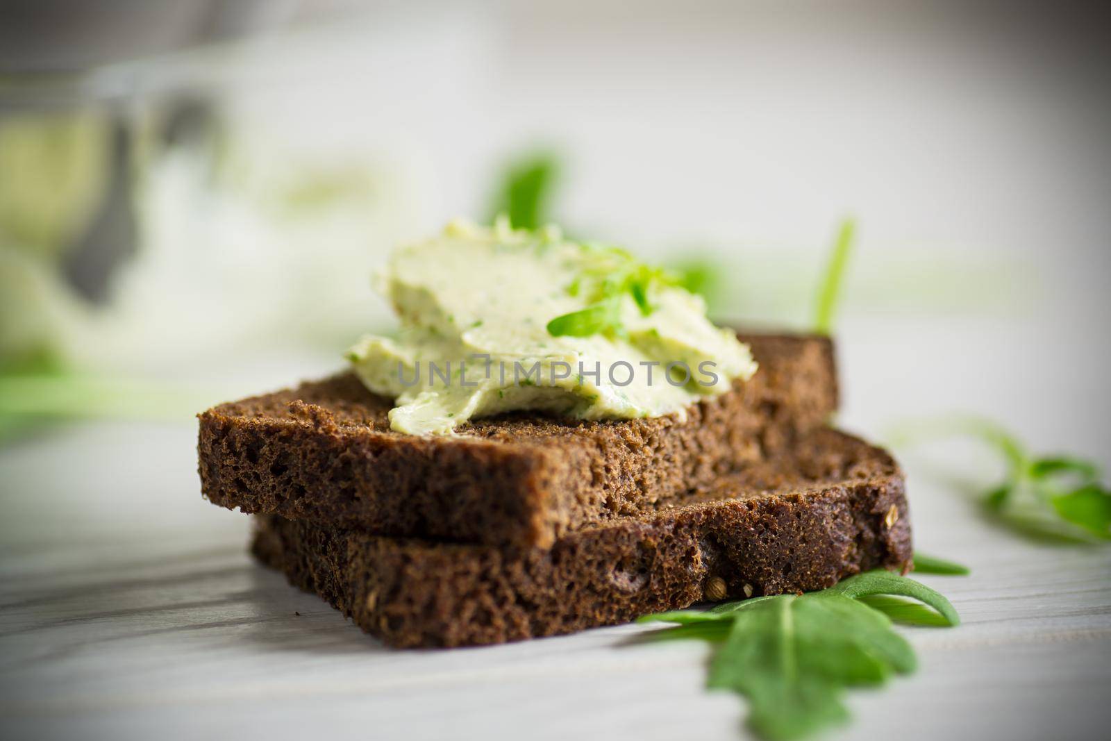 bread cheese spread with garlic and arugula on dark bread, on a wooden table.
