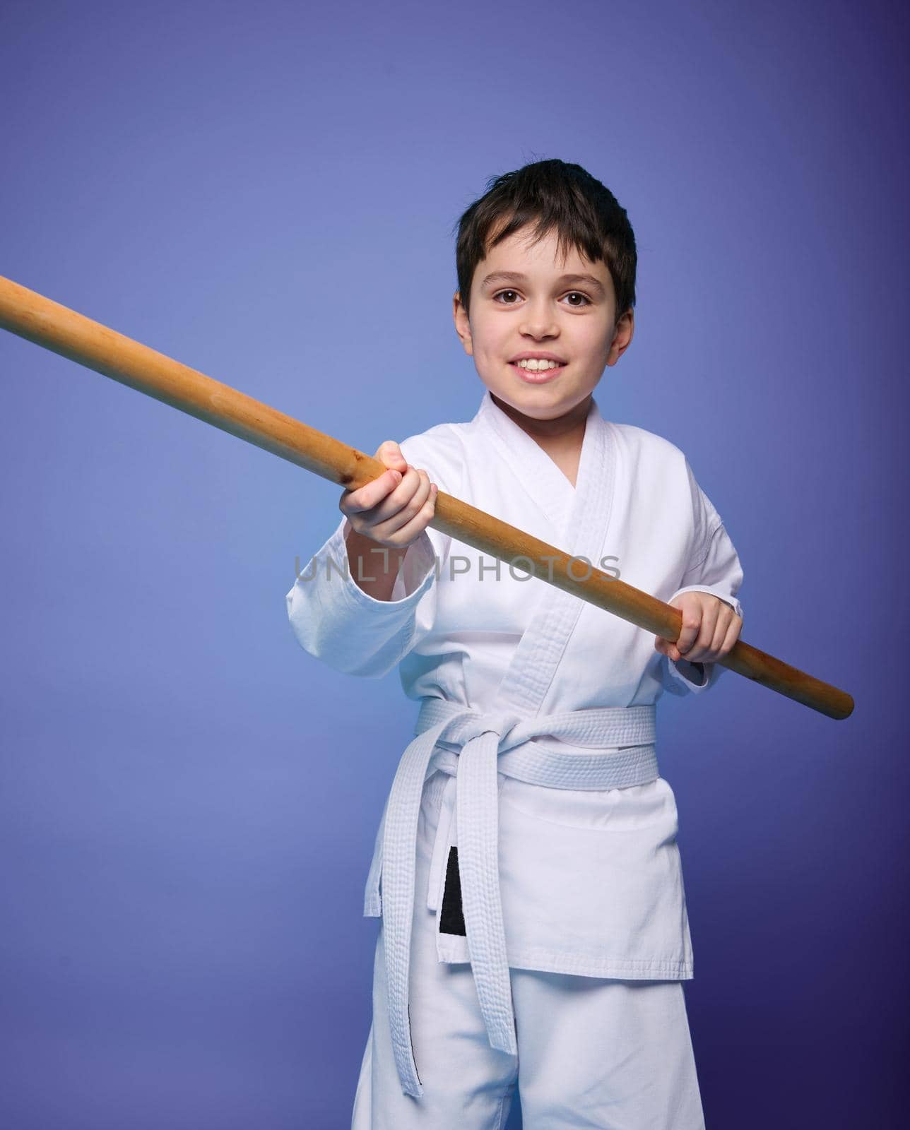 Confident strong concentrated boy - Aikido wrestler - in a kimono stands with a wooden jo weapon in his hands. Oriental martial arts practice concept