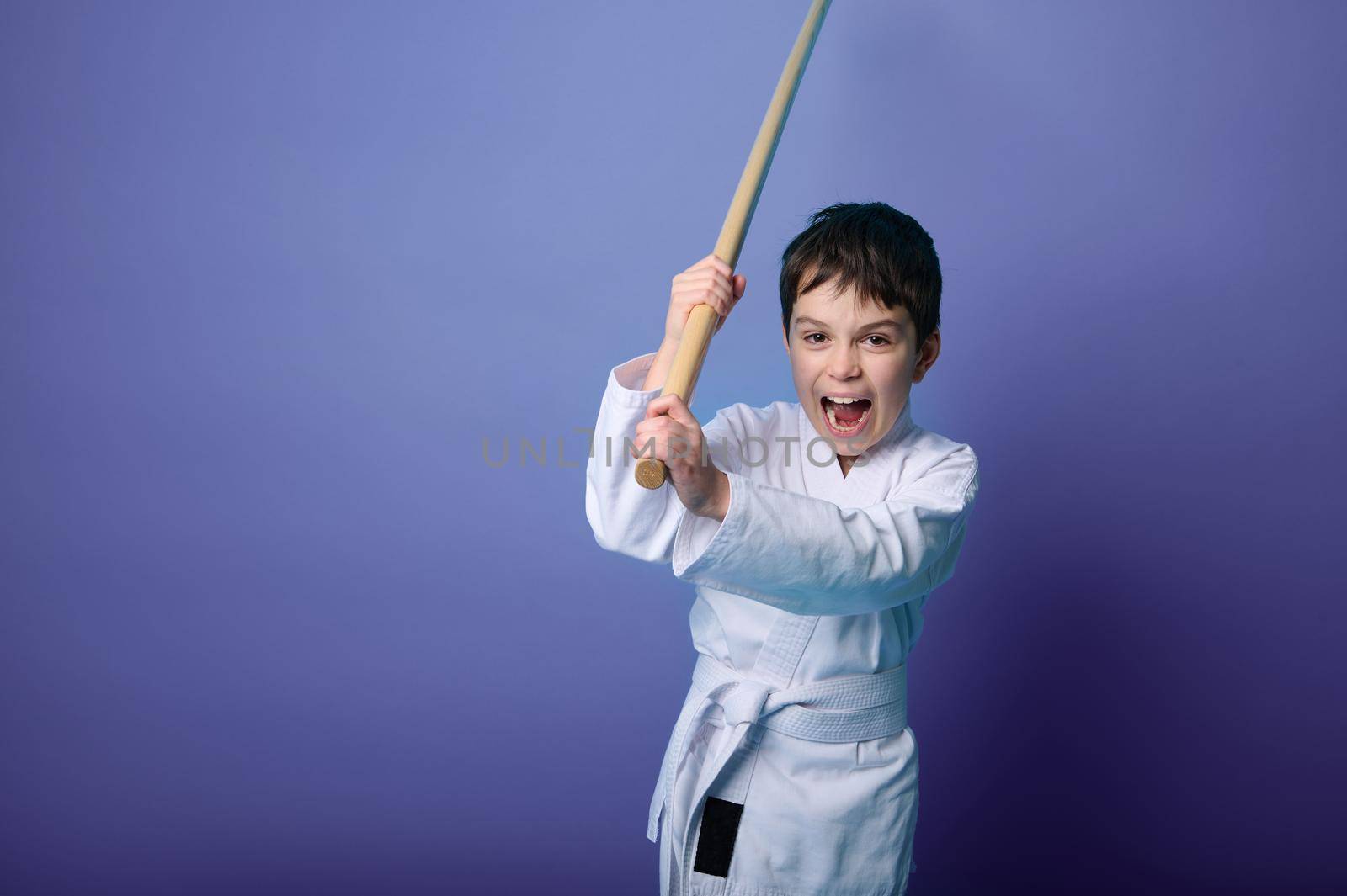 Portrait of a confident strong Caucasian child boy aikido wrestler wearing traditional samurai hakama kimono learning fight with bamboo bokken. Aikido Learning and Oriental martial arts Concept