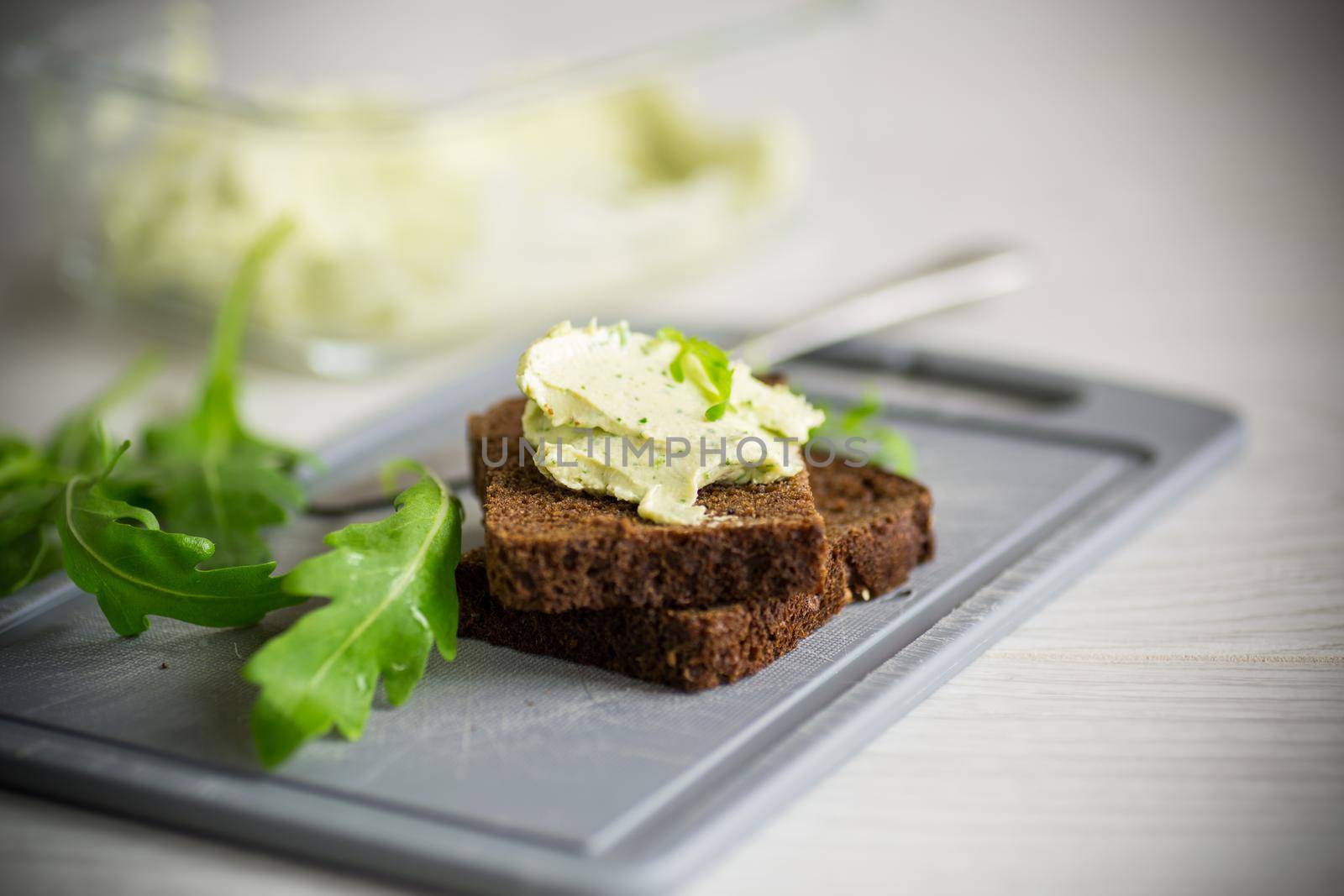 bread cheese spread with garlic and arugula on dark bread, on a wooden table.