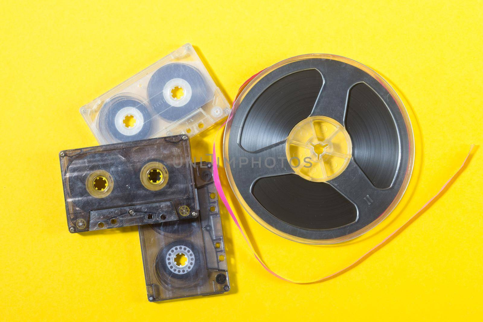 retro audio compact cassettes and reel to reel tape on a yellow background