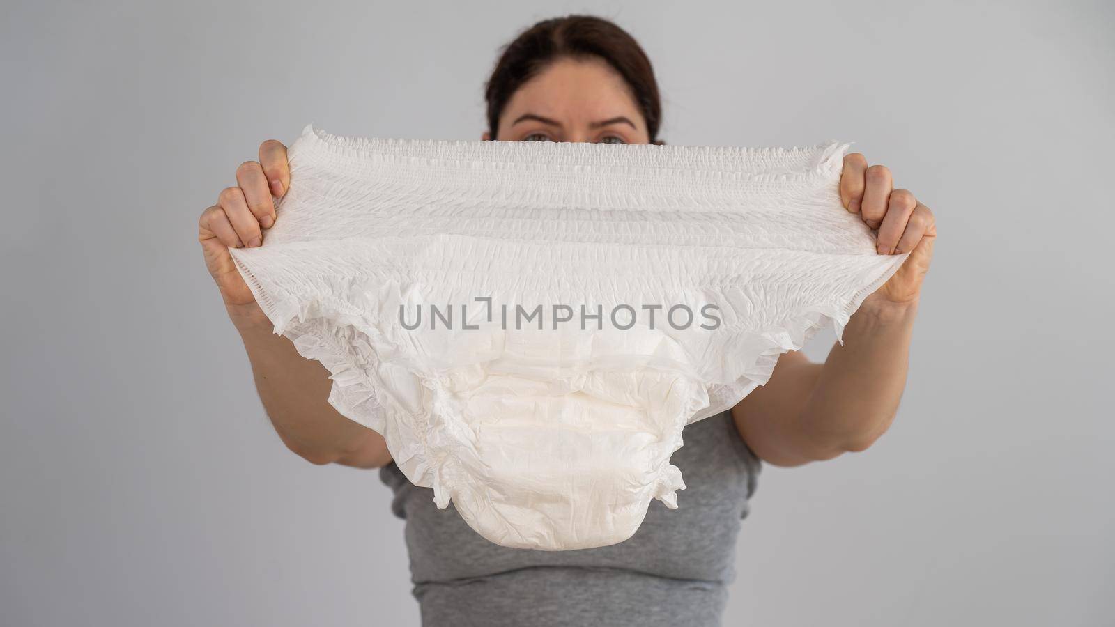 A caucasian woman holds an adult diaper and checks its strength on a white background. by mrwed54