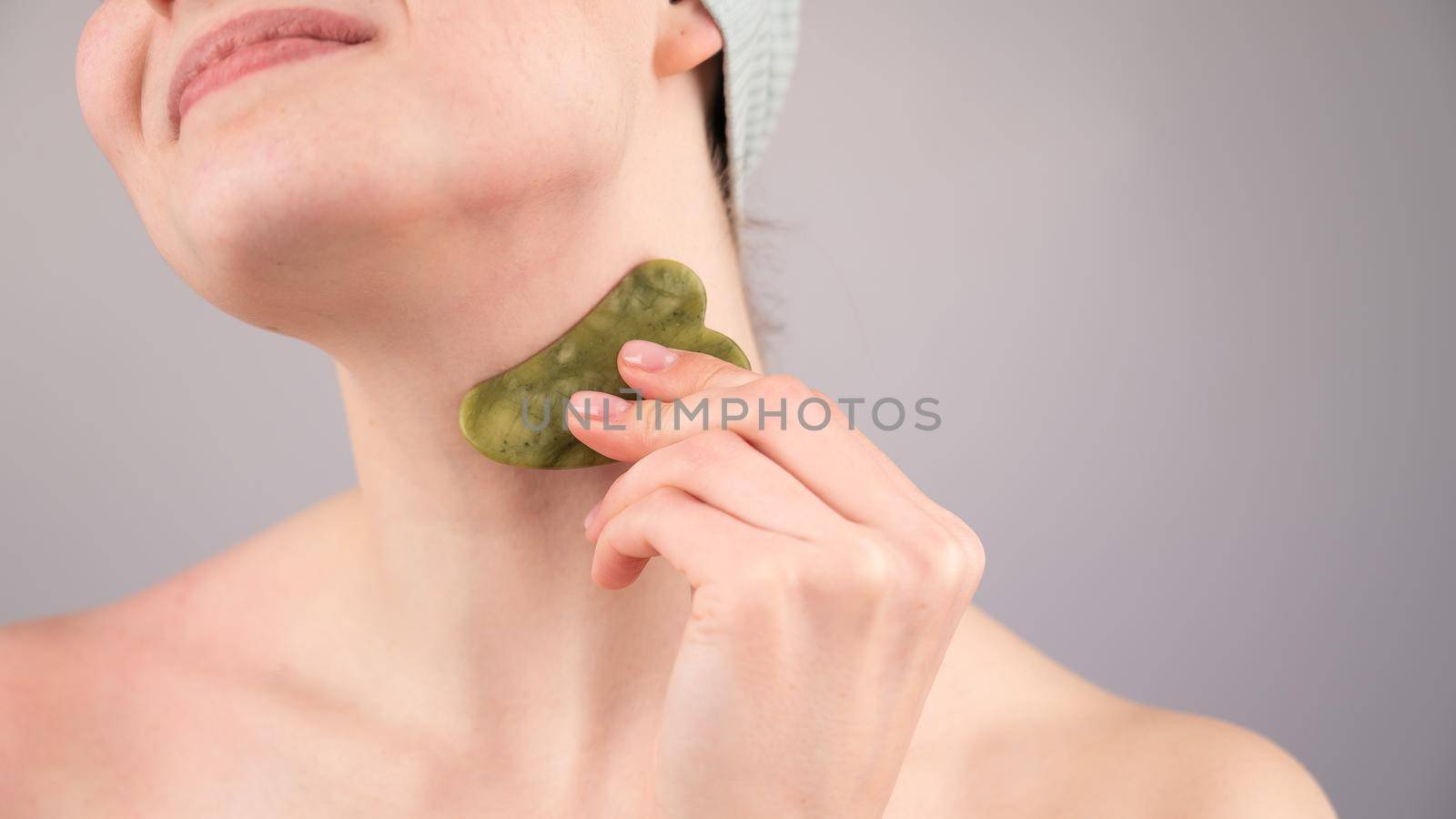 Close-up portrait of a young woman massaging her neck with a gouache scraper