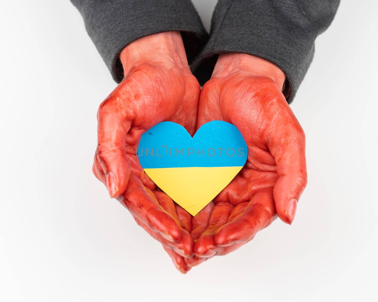 Woman with hands covered in blood holding a heart with the flag of ukraine on a white background