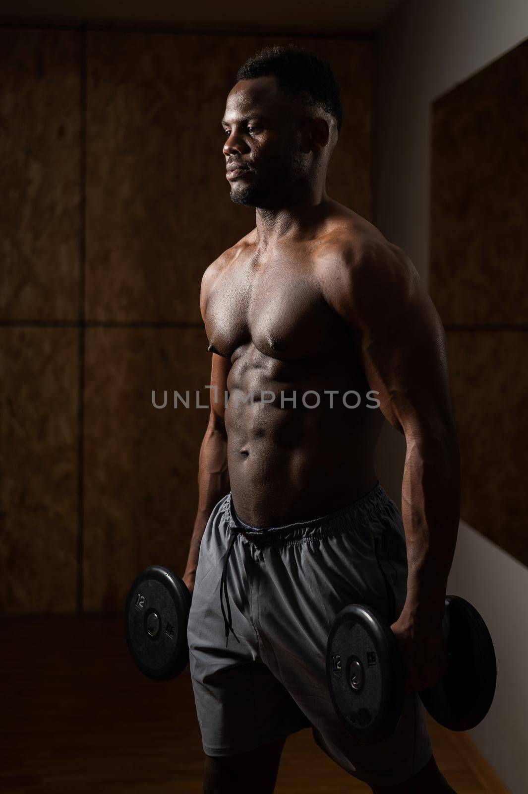 Muscular dark-skinned man doing an exercise with dumbbells. by mrwed54