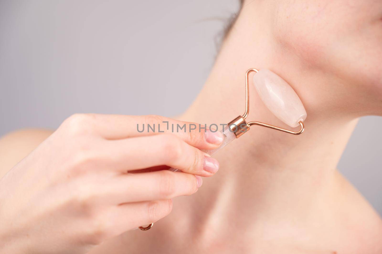 Close-up portrait of a woman using a quartz roller massager for an alternative fight against wrinkles on her neck. Smoothing of the rings of venus. by mrwed54