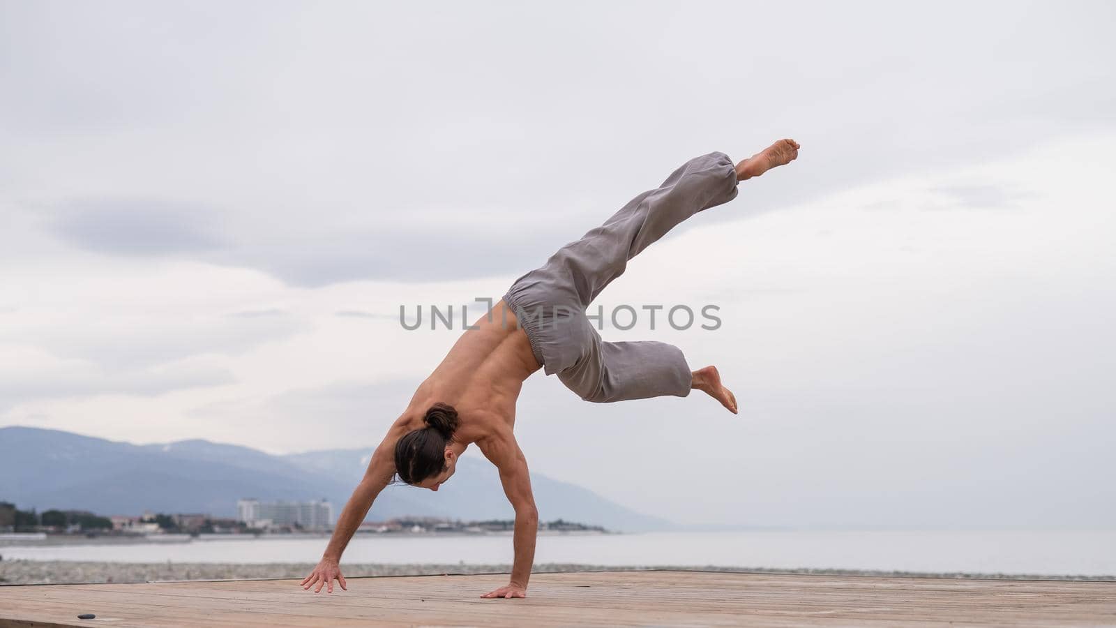 Shirtless caucasian man doing acrobatic wheel on the beach