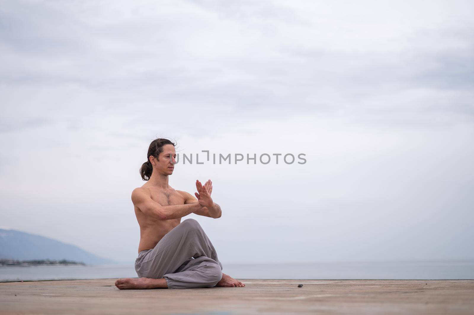 Caucasian man with naked torso practicing wushu on the seashore