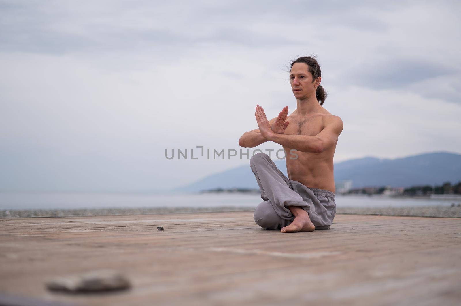 Caucasian man with naked torso practicing wushu on the seashore