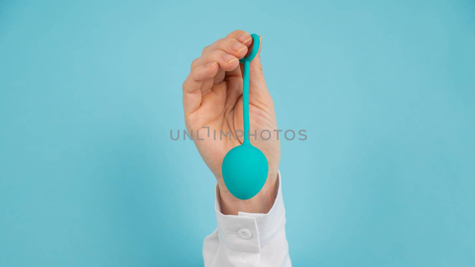 A woman's hand sticks out of a hole in a blue background and holds a vaginal egg