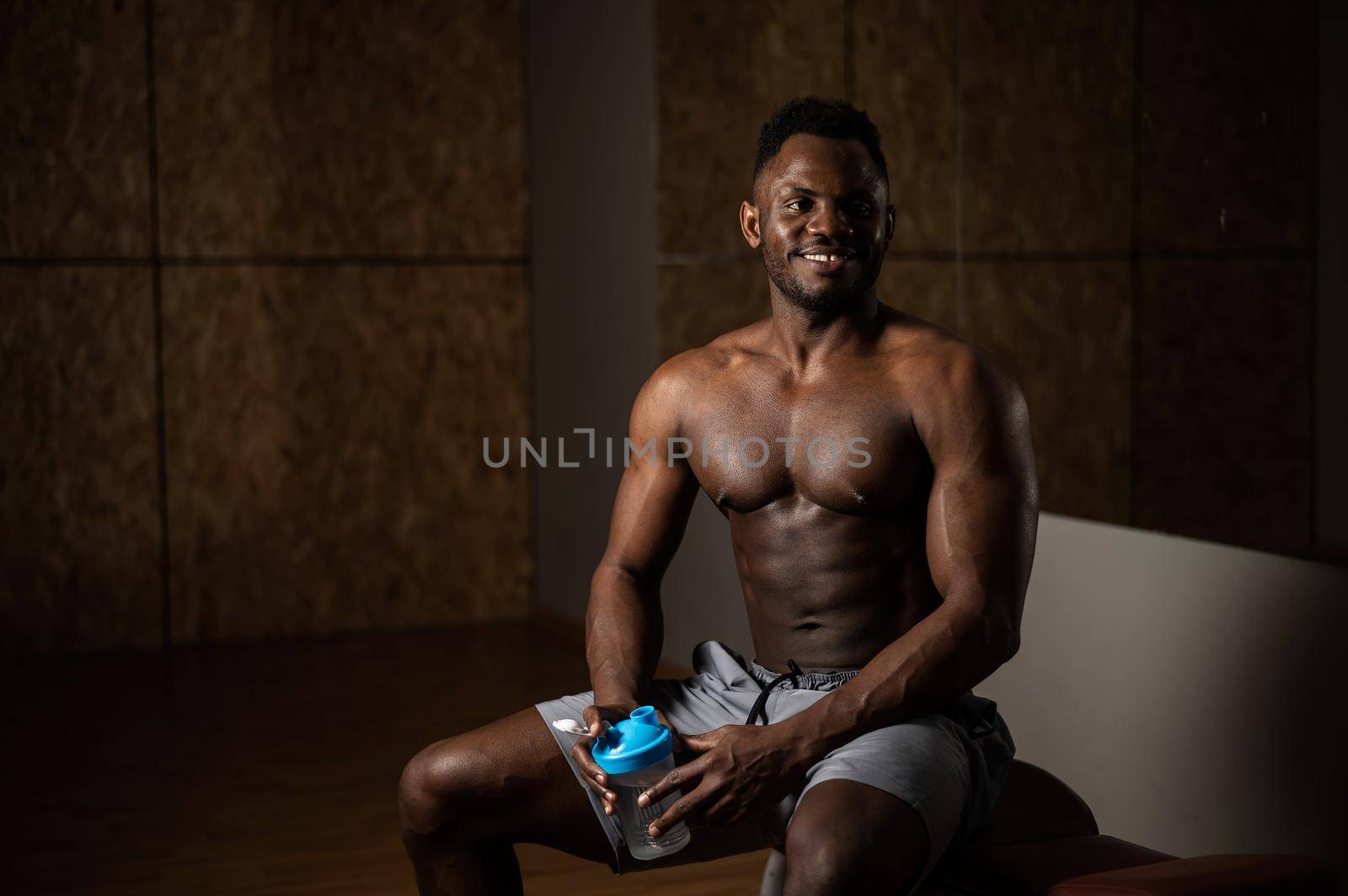 Shirtless african american man drinking from a shaker in the gym